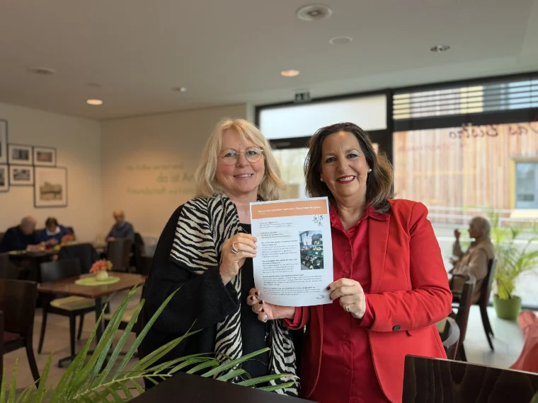 2 Frauen lächeln und halten den Newsletter aus dem Seniorenbüro in die Kamera